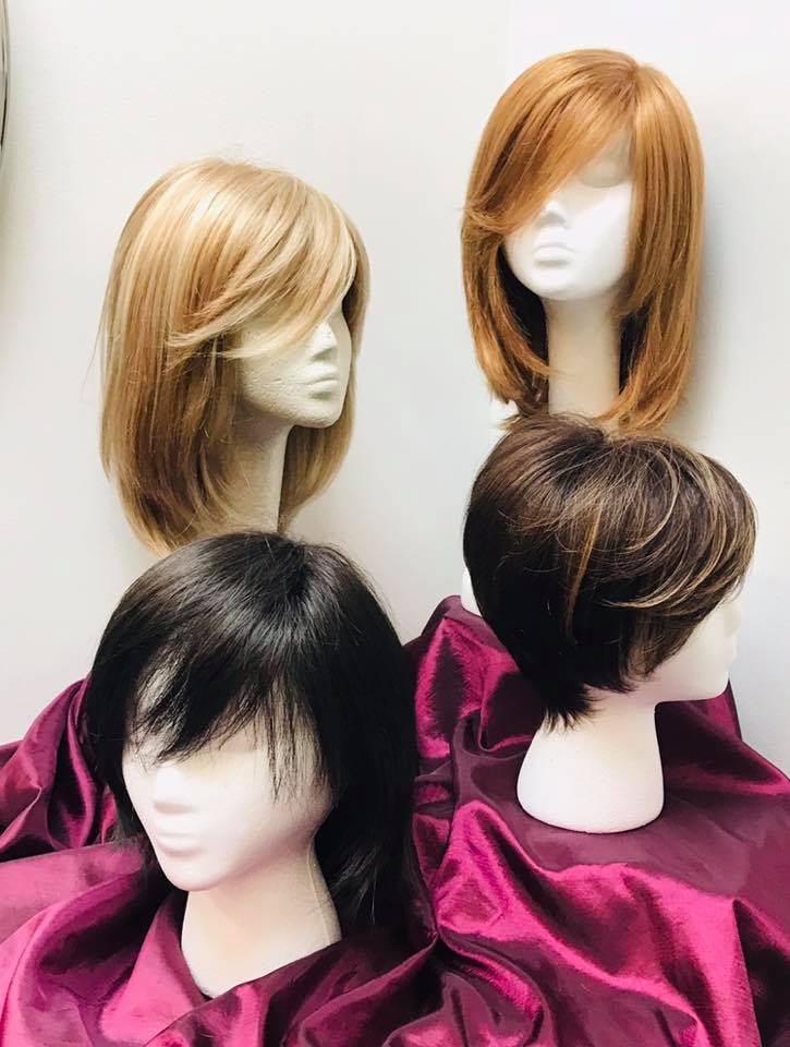 Four mannequin heads displaying various hairstyles, including blonde, red, black, and brown wigs, placed on a purple satin cloth.